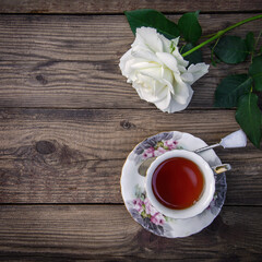 White rose and a cup of tea on a wooden background