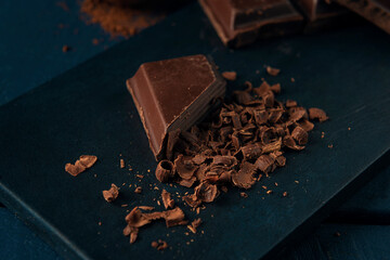 Pieces of chocolate with chocolate shavings on dark wooden table