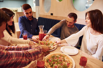 Group of young friends that sitting together indoors and eating pizza