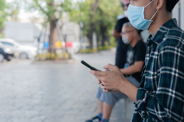 Asian man holding mobile phone sitting keep social distancing,New normal after covid 19 or Corona virus