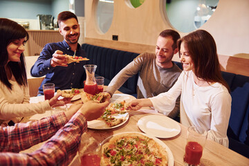 Group of young friends that sitting together indoors and eating pizza