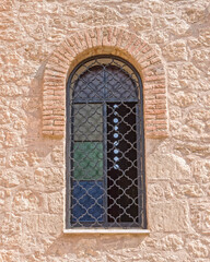 old arched window secured with iron grid on rough stone wall