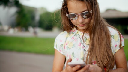 Smiling teen girl surfing internet on mobile phone in summer park.