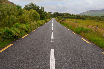 Small asphalt country road with good surface. Concept quality roadway. Mountains in the background.