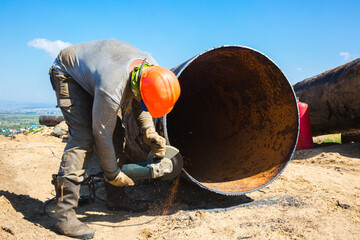 A male worker grinds the butt welding of a pipe