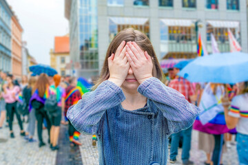 A girl stands on the street against the background of a gay parade with her eyes closed. The concept is not a desire to see and accept other people and see the problems of the lgbt community