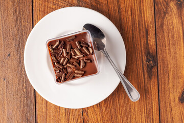 Fine chocolate dessert on a white plate with spoon on a wooden table surface.