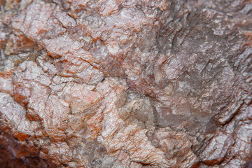 Photograph of a granite surface interspersed with transparent mica in soft focus at high magnification. Fine texture of natural mineral of pink color with blurred background.