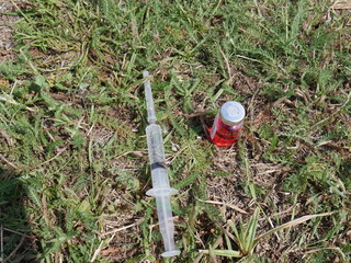 red bottle with medicine and a syringe on the background of grass
