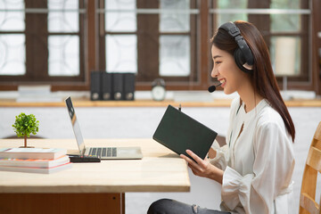 Smiling Asian young female using headset looking at laptop screen listen and learning online...
