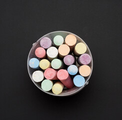 multicolored chalk in a plastic bucket on a black background