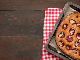 baked sponge cake with plums in a metal baking sheet on a brown wooden background