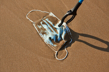 collecting a used surgical mask on the beach