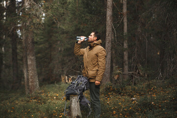 Hiker with backpack drinking water in deep forest.