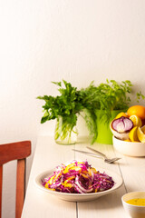 Light summer salad of red cabbage, onions and yellow bell peppers, salad in a plate on a white wooden table, olive oil with spices for dressing and basil with dill