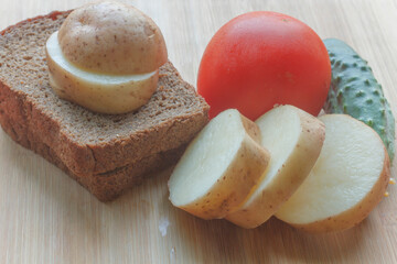 young potatoes, black bread tomato and cucumber on a wooden board 