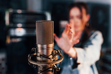 Close up view of microphone. Young beautiful female performer rehearsing in a recording studio