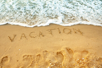 Message for the beach written with the word vacation in smooth sand with incoming wave.