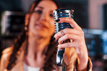 Close up view of microphone. Young beautiful female performer rehearsing in a recording studio