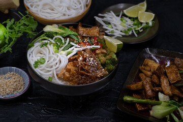 Vegan Japanese rice noodles and stir fried tofu, vegetables, soya  skins on dark table