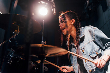 Fototapeta premium Plays drums. Young beautiful female performer rehearsing in a recording studio