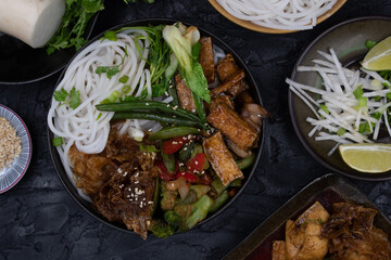 Vegan Japanese rice noodles and stir fried tofu, vegetables, soya  skins on dark table