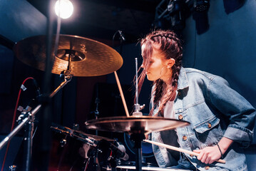 Fototapeta na wymiar Plays drums. Young beautiful female performer rehearsing in a recording studio