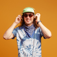 Studio portrait of a young man with long hairs in a green cap and headphones. Yellow background. Musician DJ