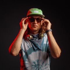Studio portrait of a young man with long hairs in a green cap and headphones. Black background. Musician DJ