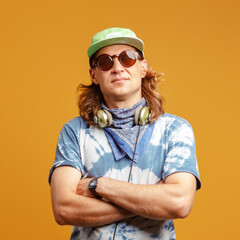 Studio portrait of a young man with long hairs in a green cap and headphones. Yellow background. Musician DJ