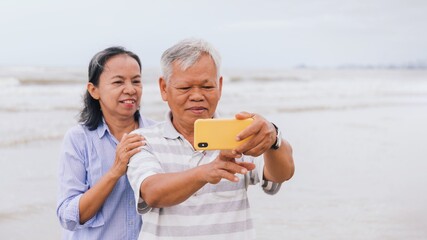 Asian old senior couples use smartphone to selfie at the beach by the sea background on weekend vacation.Concept of happy living for the elderly.
