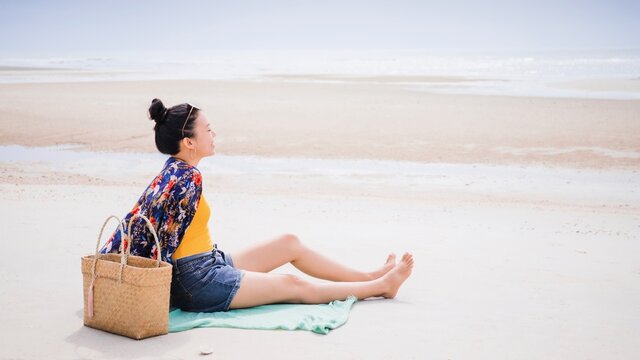 Asian Traveller Woman Sit Back And Relax On The Beach By The Sea Background On Weekend Vacation.Concept Of Happy Solo Travel.