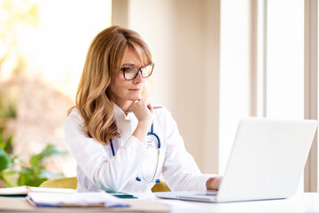 Middle aged female doctor working on laptop in doctor's room