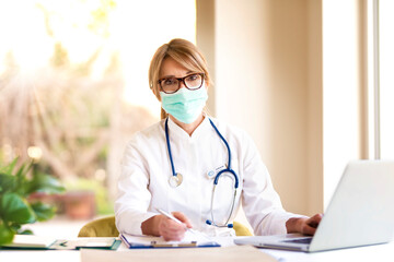 Female doctor wearing face mask while working on laptop in doctor's office