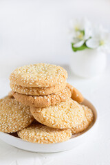 Freshly baked round sesame cookies with a apple tree flowers on a white table.