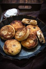 Cottage cheese pancakes, syrniki, ricotta fritters with raisins served with sour cream on a vintage plate. Dark rustic background