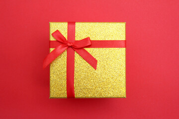 Gold gift box tied with a red bow for holidays on a red background. Gift. Top view in a flat design style. Copyspace