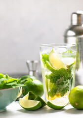Mojito cocktail with white rum, lime, brown sugar and mint. Ingredients for a Mojito cocktail. Preparation of alcoholic cocktails. Bar shaker and glass tumbler with Mojito on a light background