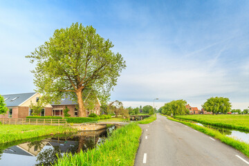 Beautiful Dutch polder landscape with channel a mansion and beautiful warm light of the rising sun with nice reflection of scenery and sky in surrounding water against clear blue sky with clouds veil