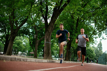 Fototapeta na wymiar Young men training on a race track. Two young friends running on the athletics track.