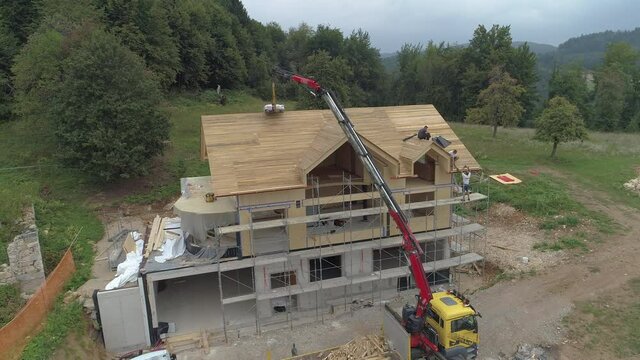 AERIAL: Truck boom reaches up to the roof of a modern prefabricated house under construction in the countryside.