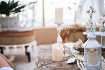 Decorate interior on an open terrace overlooking the city. In maracans, Indian, eco style in sand color: wicker furniture, macrame, lanterns with candles, glass lamps, pampas grass, poufs, a low table