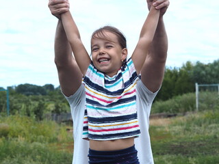 The little girl laughs with delight.Dad raises her hands up against the background of nature.