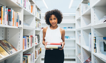 Modern woman with stack of books standing in library