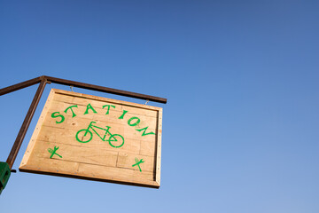 Wooden sign of a bicycle parking station, isolated against blue sky background.