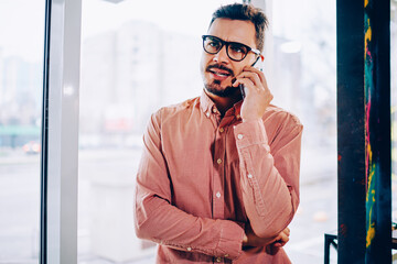 Male businessman making dissatisfied face while talking with service operator on mobile phone, young hipster guy annoyed with waiting on customer support helpline making call for solve problem.