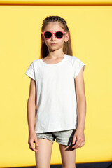 Fototapeta premium Kid girl wearing white t-shirt with space for your logo or design over yellow backdrop