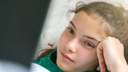 teenage brunette lies in bed and looks at black laptop