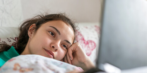 sleepy teenager with long hair lies in bed and watches movie