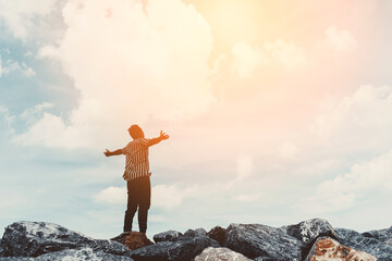 Man raise hand up at top of rock on blue sky and white cloud abstract background. Freedom feel good...